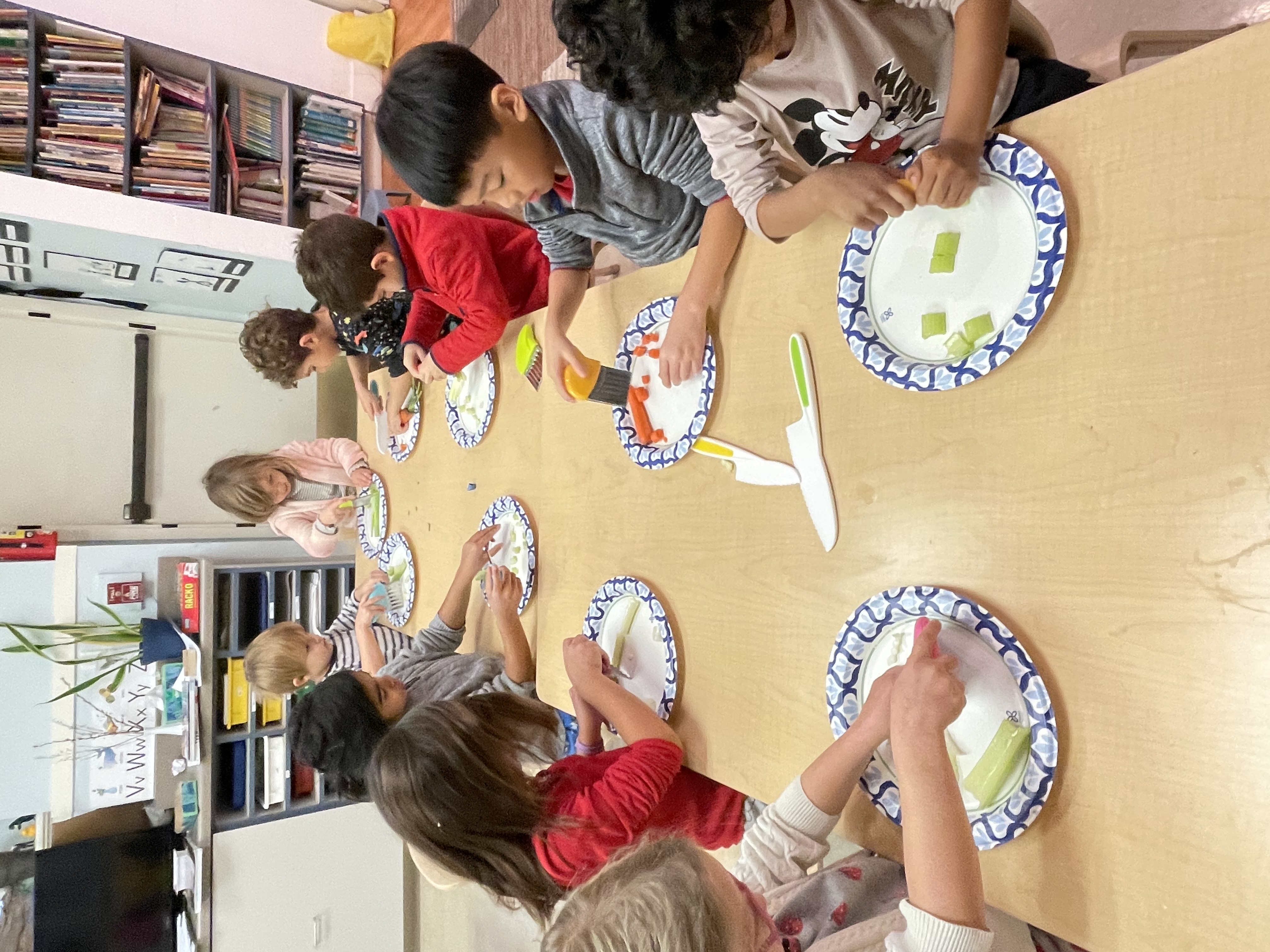 Early kindergarteners preparing vegetables together at a long table
